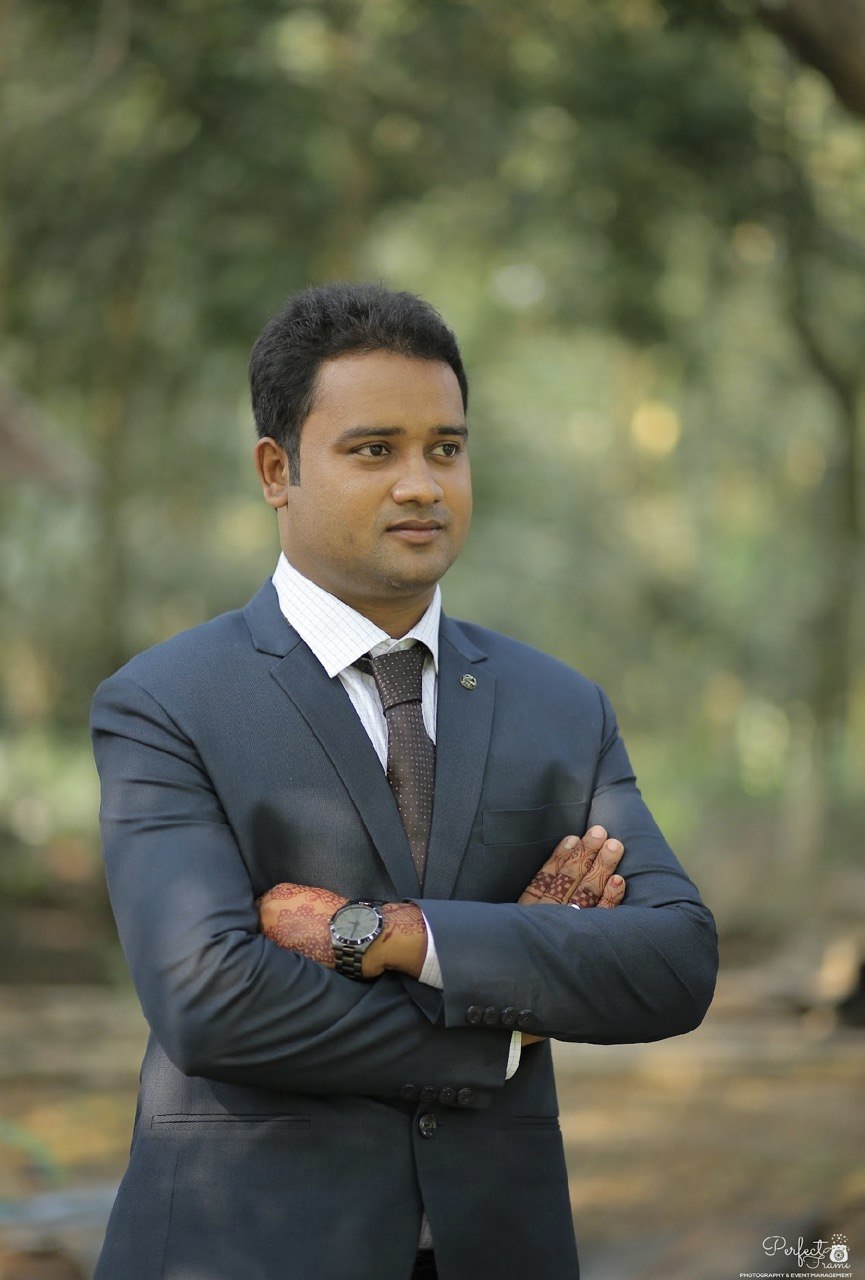 Rafiul Islam in a navy suit, standing outdoors with arms folded